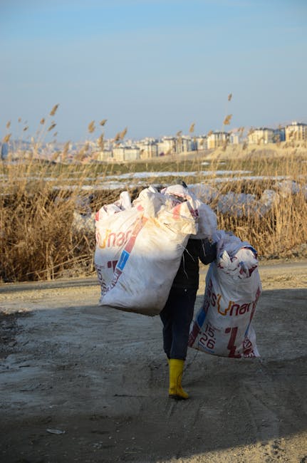 A photograph of a pile of mixed waste materials placed on a paved driveway. The pile includes large, white plastic bags, some of which are torn open revealing various unidentifiable contents, and smal