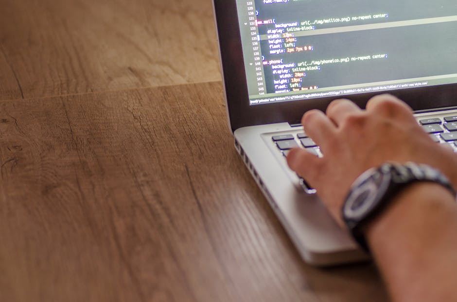 A close-up view of a laptop displaying lines of code on its screen, positioned on a wooden surface. To the right of the laptop, there is a coffee mug with a beige finish and black text that reads 'Thi